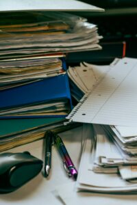 A neat and organized desk featuring stacks of paper, folders, pens, and a computer mouse.
