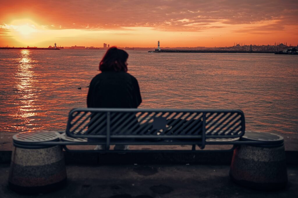 A woman sits on a bench by the sea, enjoying a serene sunset view.