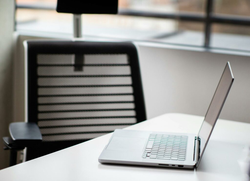 A sleek laptop on a white desk in a contemporary office setting with mesh chair.