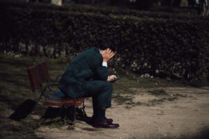 A worried businessman sits on a park bench in Madrid, holding a smartphone. Captured outdoors in natural light.