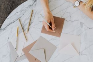 A woman's hand writing on envelopes with pencils on a marble table, top view.