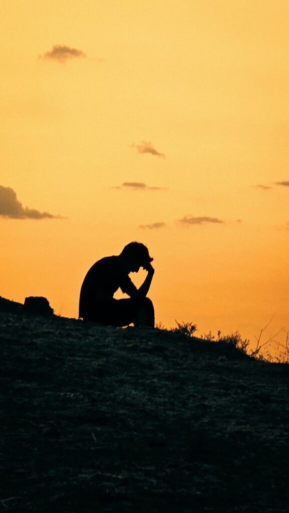 Silhouette of a person sitting on a hill against a vibrant sunset sky, evoking contemplation.