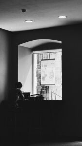 Silhouette of a person using a laptop by a window in a minimalist room, creating a calm atmosphere.