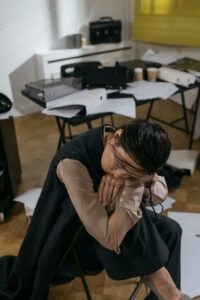 Woman in an office environment, tired and leaning on a desk, surrounded by paperwork.