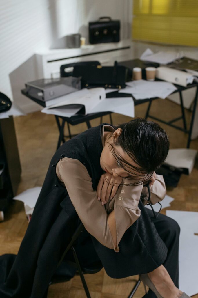 pexels-photo-6539032-6539032 Woman in an office environment, tired and leaning on a desk, surrounded by paperwork.