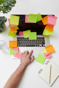 A hand reaching for a laptop surrounded by vibrant sticky notes on a tidy desk.